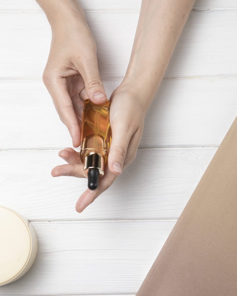 hands-holding-body-oil-white-wooden-background